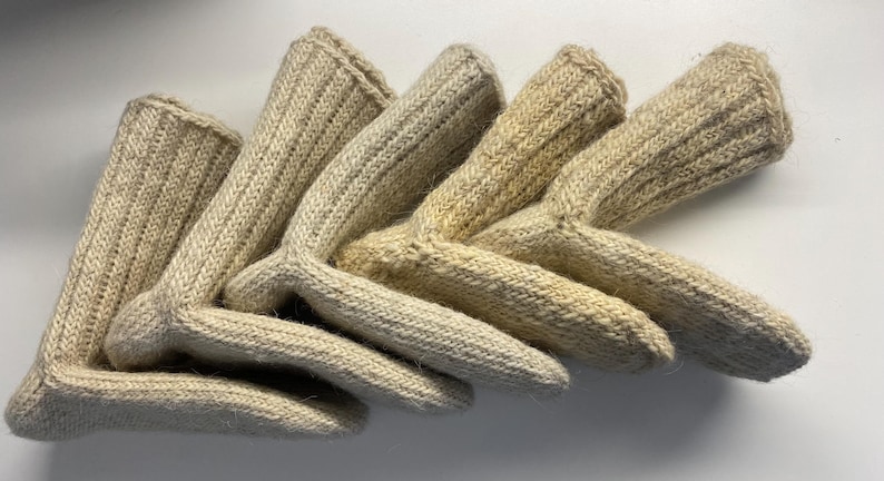 May include: A collection of beige knitted gloves, arranged in a fan shape. The gloves have a ribbed texture and a curved design at the wrist. The color is a natural, off-white hue.