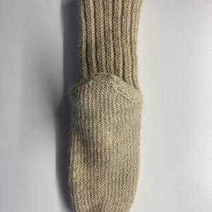 May include: A beige, ribbed-knit sock. The sock features a ribbed cuff and a rounded toe. The material appears to be a thick, warm wool or wool blend. The sock is designed to be worn on the foot.