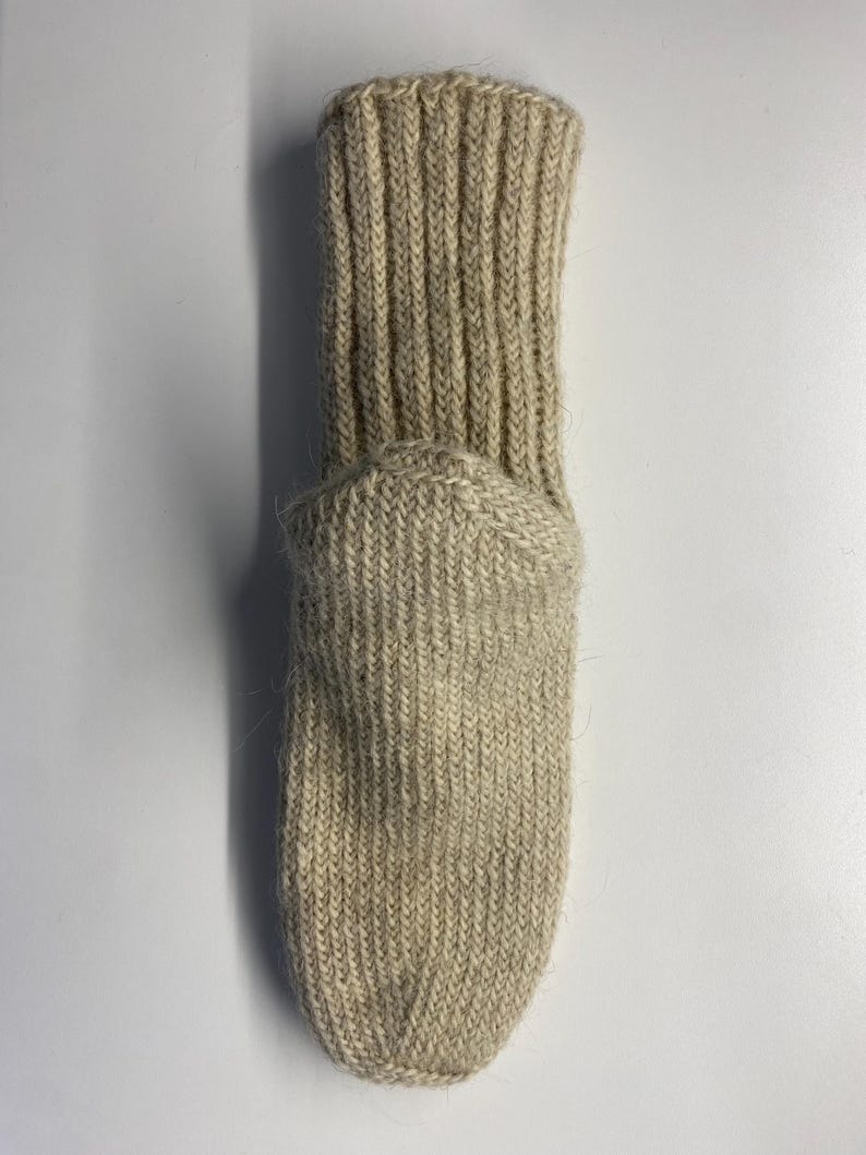 May include: A beige, ribbed-knit sock. The sock features a ribbed cuff and a rounded toe. The material appears to be a thick, warm wool or wool blend. The sock is designed to be worn on the foot.