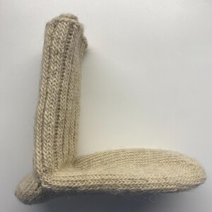 May include: A beige, hand-knitted sock with a ribbed leg and a rounded toe. The sock is made of a soft, textured yarn, and the stitches are clearly visible. The sock is lying flat on a white surface.