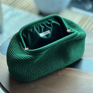 May include: A green crocheted clutch purse with a satin lining. The purse has a gold metal clasp.