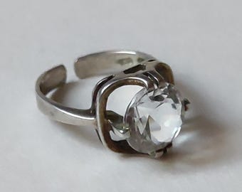 May include: A silver ring with a clear, faceted gemstone set in a geometric design.