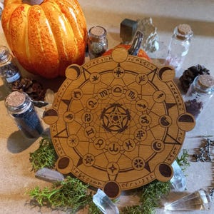 Puede incluir: Un tablero circular de madera con un pentagrama en el centro y símbolos astrológicos alrededor. El tablero está rodeado por un anillo de fases lunares.