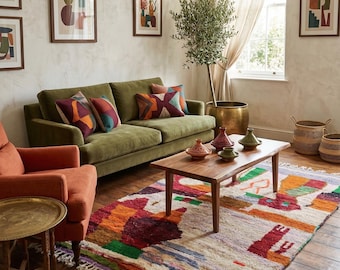 May include: A living room scene featuring a green sofa with patterned pillows, an orange armchair, and a colorful rug. A wooden coffee table displays decorative vases. Artwork hangs on the wall, and a potted olive tree adds a natural touch.