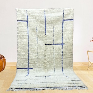 May include: A white and blue geometric patterned rug with a fringe border. The rug has a light cream background with blue lines forming a geometric pattern.
