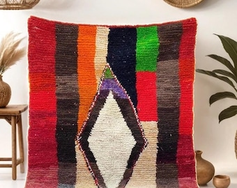 May include: A colorful Moroccan rug with a diamond pattern in the center. The rug has stripes of red, orange, green, black, and white. The rug is on a blue rug.