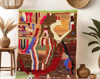 May include: A colorful, abstract rug with a geometric design in shades of red, orange, yellow, blue, green, and brown. The rug has a fringe border and is hanging on a white wall.