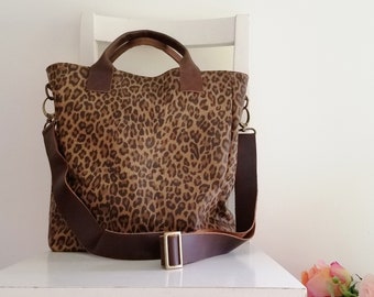 May include: A tote bag with a leopard print pattern. The bag has brown leather handles and a matching adjustable shoulder strap. The bag features a gold-colored buckle and hardware.