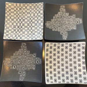 May include: Four square ceramic plates with unique black and white designs. One plate features a checkerboard pattern, two have an abstract geometric design, and the last has a pattern of squares with circles.