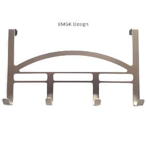 Puede incluir: Gancho plateado para colgar en la puerta, con cuatro ganchos y una barra superior curva. El gancho está etiquetado como "EMGK Design".