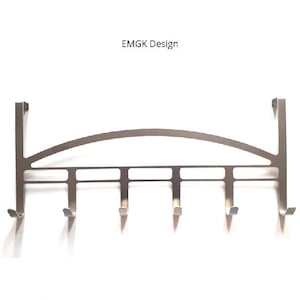 Puede incluir: Un perchero plateado para colgar sobre la puerta con seis ganchos. El perchero tiene una parte superior curvada y el texto "EMGK Design" está encima.