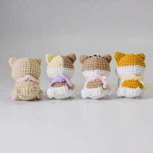 May include: Four crocheted stuffed animals in the shape of dogs. The dogs are all white with different colored patches on their backs. They are wearing crocheted scarves in different colors.
