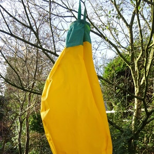 May include: A yellow and green fabric pouch hanging from a tree branch. The pouch is shaped like a banana and has a green top.