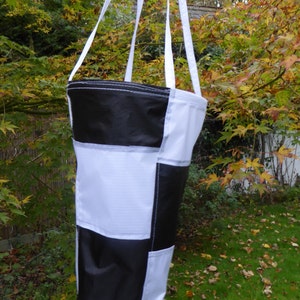 May include: A black and white chequered windsock hanging from a tree branch. The windsock is made of fabric and has a cylindrical shape.