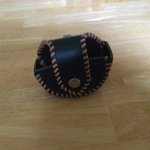 May include: A black leather coin purse with brown stitching and a silver snap closure.