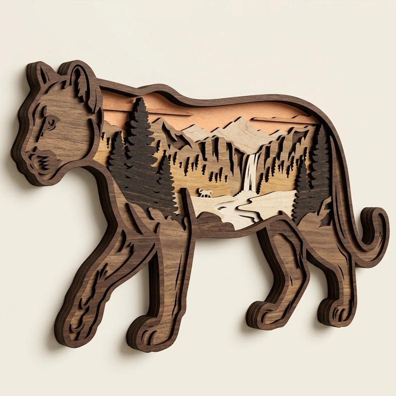 May include: A multi-layered wooden wall art piece shaped like a mountain lion. The dark wood silhouette frames a detailed landscape featuring layered pine trees, jagged mountain peaks, a flowing waterfall, and a small animal figure in the center.