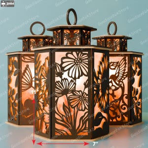 Puede incluir: Conjunto de tres faroles decorativos de metal con intrincados diseños florales e insectos. Cada farol mide aproximadamente 18 cm de ancho y 18 cm de alto. Los faroles emiten un brillo cálido, ideal para crear ambiente.