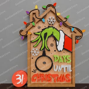 May include: Wooden Christmas countdown calendar featuring a Grinch hand design. The calendar includes the text "Days Until Christmas" and "31" on a separate circle. The house-shaped design is adorned with colorful lights and snowflakes.