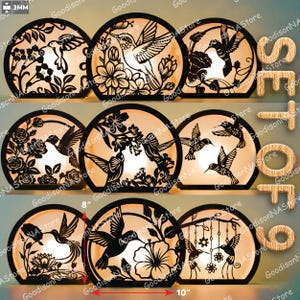 May include: Set of nine decorative hummingbird lamps. Each lamp features a black, laser-cut hummingbird design with floral accents. The lamps are approximately 10 inches wide and 8 inches tall, with a warm, glowing interior.