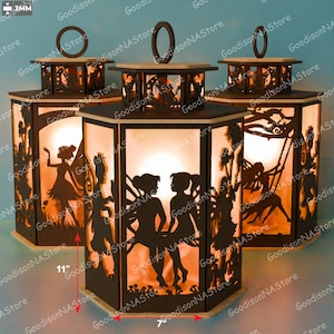 May include: Hexagonal wooden lanterns with fairy silhouettes, each 28 cm tall and 18 cm wide. The lanterns have a warm, glowing interior and a handle on top. The sides feature intricate cut-out designs of fairies and trees.