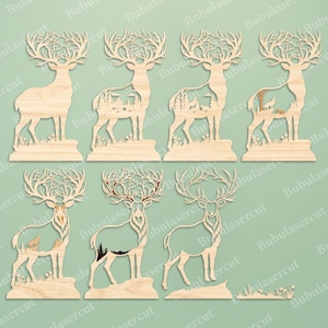 May include: A collection of seven light-colored wooden deer silhouettes featuring intricate laser-cut designs. Each deer displays detailed antlers and various cut-out forest scenes, including mountains, trees, and wildlife, with one deer left blank.