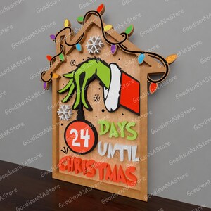 May include: Wooden Christmas countdown sign featuring a Grinch hand holding a Christmas ornament. The sign reads "24 Days Until Christmas" in colorful 3D letters. Decorative lights and snowflakes adorn the top of the sign.