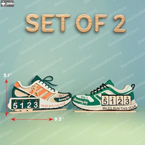 Puede incluir: Un juego de dos contadores de millas con forma de zapatilla de correr de madera. Una zapatilla es blanca, naranja y verde, la otra es verde y blanca. Cada una tiene un contador que muestra "5123" y el texto "Miles Run This Year". También está presente el texto "Alex's Running log".
