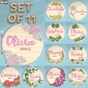 May include: Set of 11 wooden name signs, each 12 inches in diameter. The signs feature names like Olivia, Charlotte, and Emma, with floral and botanical designs. The names are in pink, with the word "Set of 11" at the top.