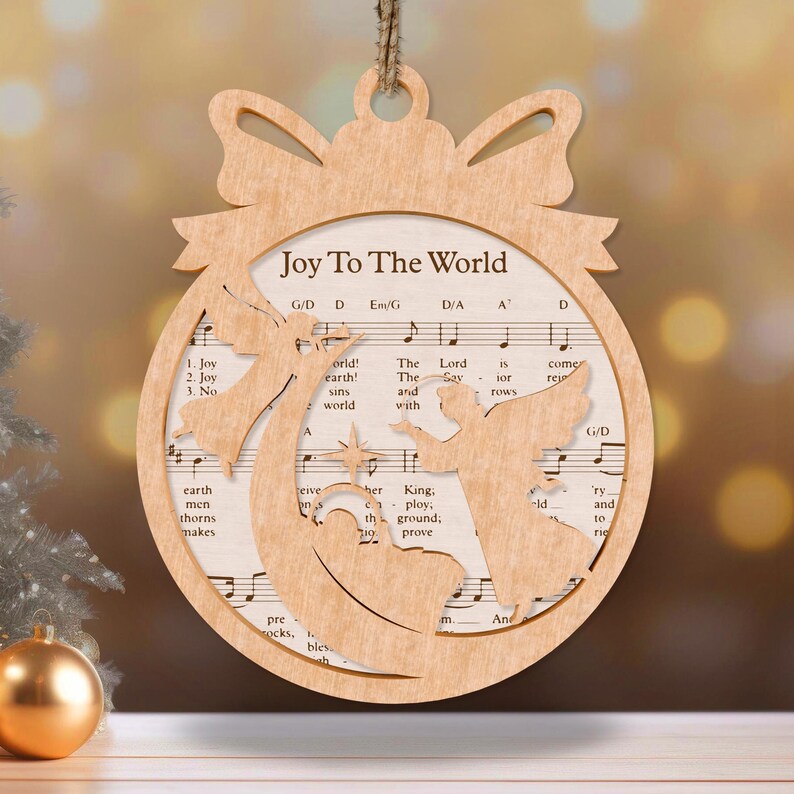 May include: A wooden Christmas ornament shaped like a ball with a bow at the top. The ornament is decorated with a silhouette of angels and the words "Joy To The World".