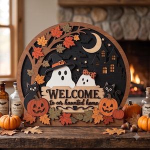 Peut inclure: Une enseigne en bois en arc de cercle superposé représentant une scène d'Halloween avec deux fantômes blancs, dont un portant un chapeau, deux chats noirs et deux citrouilles orange. Le texte central indique WELCOME to our haunted home.