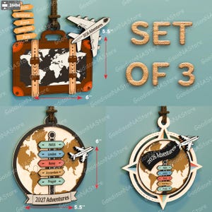 Op de afbeelding: Een set van drie houten ornamenten met een reisthema. Eén is een koffer met een wereldkaart, een ander een wereldbol met stadsborden en de laatste een kompas. Elk ornament bevat een vliegtuig en de tekst "2026 Adventures" of "2027 Adventures". De koffer is 15 cm breed.