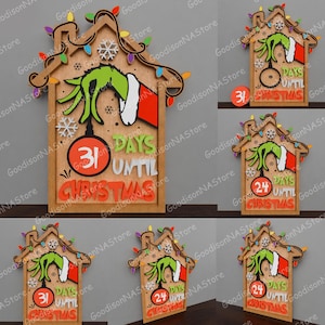 May include: Wooden Christmas countdown sign featuring a Grinch-themed design. The sign is shaped like a house and includes a green hand, a red and white sleeve, and the text "31 Days Until Christmas". The sign is decorated with lights and snowflakes.