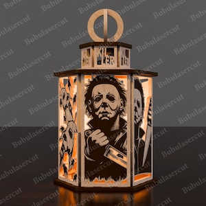 May include: A wooden Halloween lantern featuring laser-cut images of Michael Myers and other horror-themed figures. The lantern has a hexagonal base and a decorative top with the word "KILLER" cut out. The design includes orange and brown tones.