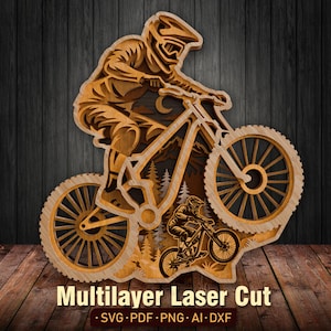 Könnte beinhalten: Ein mehrschichtiges Wandkunstobjekt aus Holz, das einen Mountainbiker mit Helm auf einem Fahrrad zeigt, mit einer kleineren Mountainbiker-Silhouette darunter vor einem Waldhintergrund. Das Design enthält den Text Multilayer Laser Cut SVG PDF PNG AI DXF.