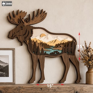 May include: A layered wooden moose wall art piece featuring a mountain landscape, forest, and river cutout. The design includes a 3mm thickness indicator and 15-inch height and width dimensions marked with red arrows on the object.