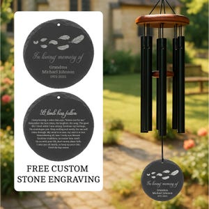 May include: A memorial wind chime featuring black metal tubes suspended from a wooden top, paired with a round, dark gray stone plaque engraved with feather illustrations and the text In loving memory of Grandma Michael Johnson 1975-2025.