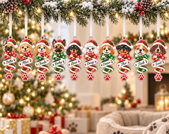 May include: Ten hanging Christmas ornaments featuring various dog breeds wearing Santa hats and red and green scarves. Each ornament displays a name: Bella, Max, Charlie, Rocky, Luna, Daisy, Cooper, Thor, Tank, and Scout, with a red paw print at the base.