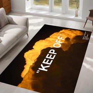 Può includere: Un tappeto nero e giallo con un design a nuvole bianche e il testo "KEEP OFF" in lettere bianche.