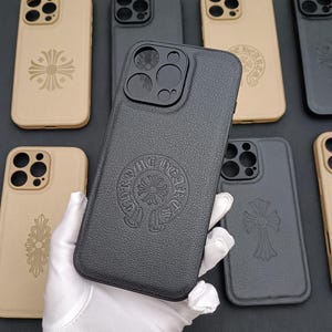 May include: A collection of phone cases with different designs. The cases are black, brown, and beige. The designs include a cross with a circle around it, and a cross with a circle around it with the words "Chrome Hearts" written around it.