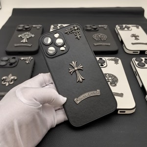 Puede incluir: Una colección de fundas para teléfono de color negro y blanco con un diseño de cruz y las palabras "Chrome Hearts" en la funda negra.