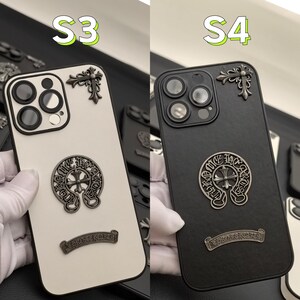 Puede incluir: Dos fundas para tel&eacute;fono con un dise&ntilde;o en blanco y negro. Las fundas presentan una cruz y una herradura con las palabras "Chrome Hearts" impresas en ellas. La funda de la izquierda es blanca y la funda de la derecha es negra.