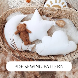May include: A PDF sewing pattern for a set of three plush pillows shaped like a crescent moon, a star, and a cloud. The pillows are white and are displayed in a wicker basket with a brown teddy bear.