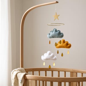 May include: A wooden mobile stand with a white, blue, and yellow felt cloud mobile hanging from it. The mobile also features a gold star and gold raindrops.