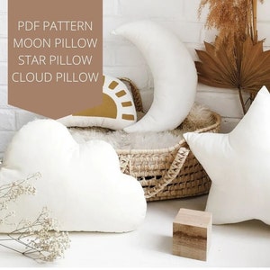 Può includere: Modello PDF per un cuscino a forma di luna, stella e nuvola. I cuscini sono bianchi e sono disposti su un cesto di vimini. Il testo "PDF PATTERN MOON PILLOW STAR PILLOW CLOUD PILLOW" è visualizzato su un rettangolo marrone.
