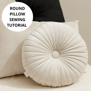 Könnte beinhalten: Ein rundes, cremefarbenes Kissen mit Knopfheftung. Das Kissen ist aus einem weichen, strukturierten Stoff.