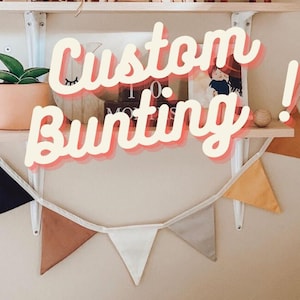 Peut inclure: Une guirlande de fanions blancs avec des fanions de différentes couleurs et motifs, dont le marron, le jaune, le blanc et le noir. La guirlande est suspendue à une étagère avec le texte "Custom Bunting!" en lettres roses.