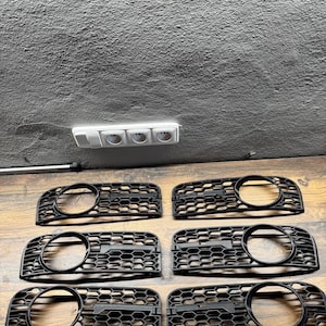 Peut inclure: Six inserts de calandre de voiture en plastique noir avec un motif en nid d'abeille. Les grilles ont une ouverture ronde au centre.