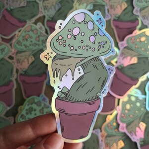 May include: A holographic sticker of a green mushroom with white spots growing out of a pot. The mushroom has a dripping, gooey substance coming from the top.
