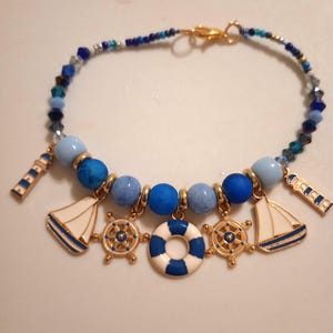 May include: A nautical-themed bracelet featuring blue and gold charms. The bracelet includes charms of sailboats, ship wheels, and a life preserver. The bracelet is made with blue beads and a gold clasp.