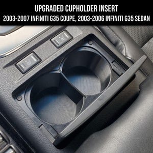 Może przedstawiać: Zbliżenie na czarną konsolę środkową samochodu z wkładką do kubków. Wkładka ma dwa uchwyty na kubki i przesuwaną osłonę. Konsola ma również dwa przyciski z symbolami ogrzewania siedzeń.